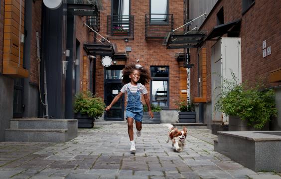 Child running alongside dog in city environment