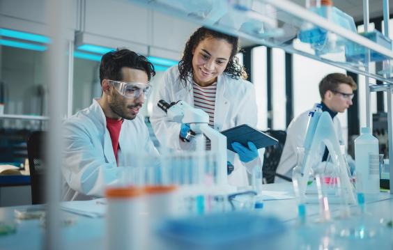 Modern Medical Research Laboratory, Young Scientists Using Microscope, Digital Tablet, Doing Sample Analysis, Talking. Diverse Team of Specialists work in Advanced Lab.