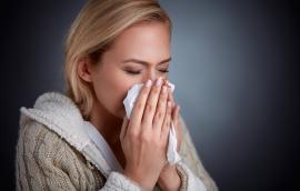 A woman sneezes into a tissue.