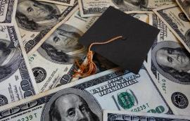 A graduation cap lies amongst $100 bills.