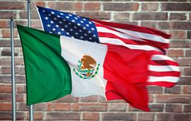 The Mexico and U.S. flags in front of a brick wall.