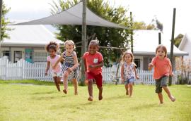 Five children run across a lawn.