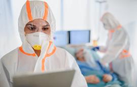 Healthcare workers wear hooded coveralls and masks while interacting with patients.