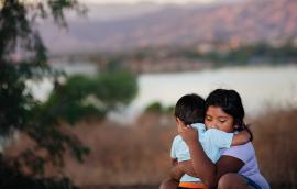 Brother and sister separated from parents are hugging each other in a foreign country, across a river. 