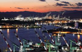 Night view of shipyard with tower cranes near the sea against chimney of oil refinery factory.