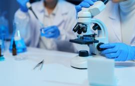 Medical researchers wearing lab coats and gloves are using a microscope and pipette, conducting experiments and research in a modern laboratory setting with beakers and tweezers.