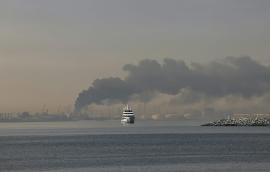 A yacht sails past a plume of smoke rising from the port of Jebel Ali following a reported Iranian strike in Dubai on March 1, 2026.