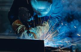 Industrial welder at work with sparks flying in shipyard setting.
