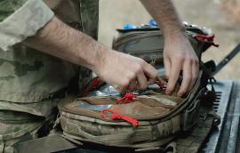  Military paramedic hands near open backpack with first aid kit, close up