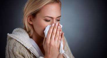A woman sneezes into a tissue.