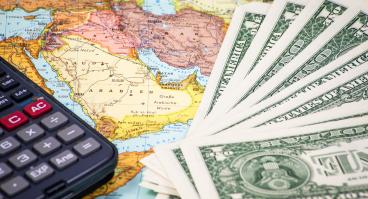 Money and a calculator rest on top of a map of the Middle East.