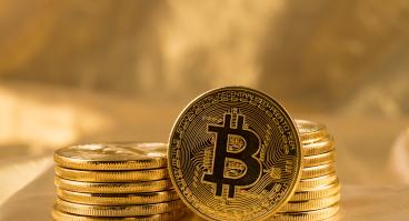 A Bitcoin leans against two stacks of Bitcoins.