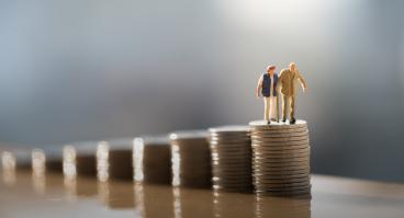 Two old people standing on a stack of coins.