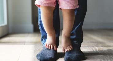 A child stands on parent's feet.