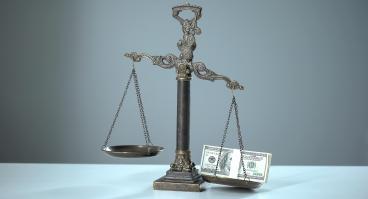 Money weighs down a balance scale.