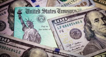 A stimulus check lies amongst hundred dollar bills.