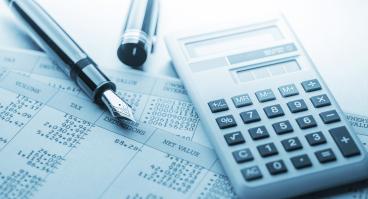 A calculator and fountain pen lie on top of accounting documents.