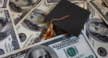 A graduation cap lies amongst $100 bills.