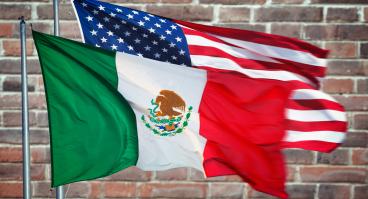 The Mexico and U.S. flags in front of a brick wall.