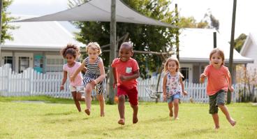 Five children run across a lawn.