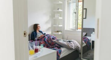 A woman lies in bed while looking out a window.