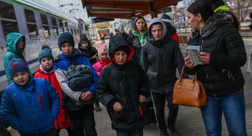 Ukrainian refugees walk down a street with their belongings.