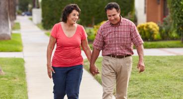 A Hispanic senior couple walks through a neighborhood.