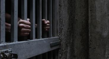 A prisoner grabs onto the bars of a jail cell.