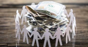 Paper cut-outs of people surrounding a pile of cash.