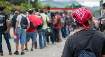 Line of Hispanic immigrants waiting outside with backs to viewer.