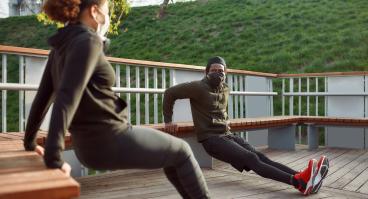 Two individuals in masks doing tricep exercises outdoors.