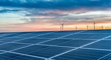Solar panels with wind turbines in the distance at sundown.