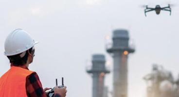 person in safety vest flying drone near power plant