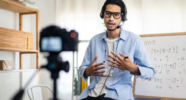 A teacher records a video for a remote class in front of a camera.