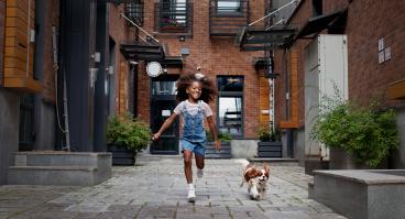 Child running alongside dog in city environment