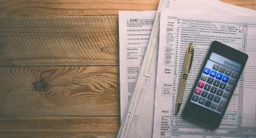 tax forms on table with calculator and pen on top