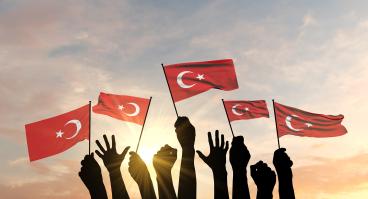 Turkish flags held up by hands against the sky