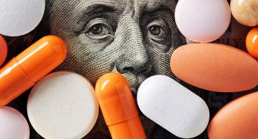 Capitalism and healthcare policy concept. Colorful medical pills cover Benjamin Franklin's face on one hundred American dollar bill. Macro top down view.