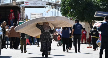 A woman carries a mattress over her head as she enters Syria from Lebanon via the Jusiyeh border crossing with Quseir in Syria's central Homs province on October 2, 2024.