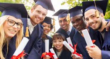 Smiling young graduates in gowns and mortarboards clutching diplomas
