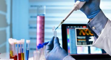 Scientist holding tube and working with laptop at genetic lab 