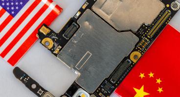 Micro chips and parts of a cellphone in between the American and Chinese national flags
