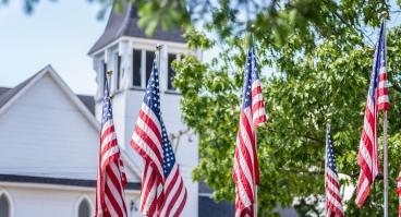 American flags waving outside old white church building