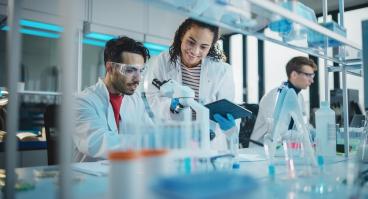 Modern Medical Research Laboratory, Young Scientists Using Microscope, Digital Tablet, Doing Sample Analysis, Talking. Diverse Team of Specialists work in Advanced Lab.
