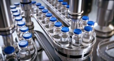 Closeup of ampules are being filled with vaccine and closed with blue caps.