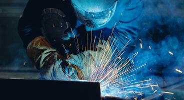 Industrial welder at work with sparks flying in shipyard setting.