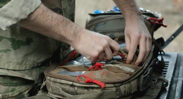  Military paramedic hands near open backpack with first aid kit, close up