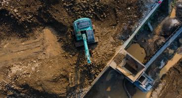 Excavator in Mining Quarry and Rock Crusher Facility on Sunny Day, Industrial mining site captured from above, featuring heavy machinery, material processing operations, rugged excavation terrain