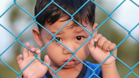 A child refugee stands behind a fence.