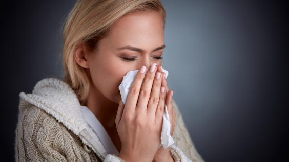 A woman sneezes into a tissue.